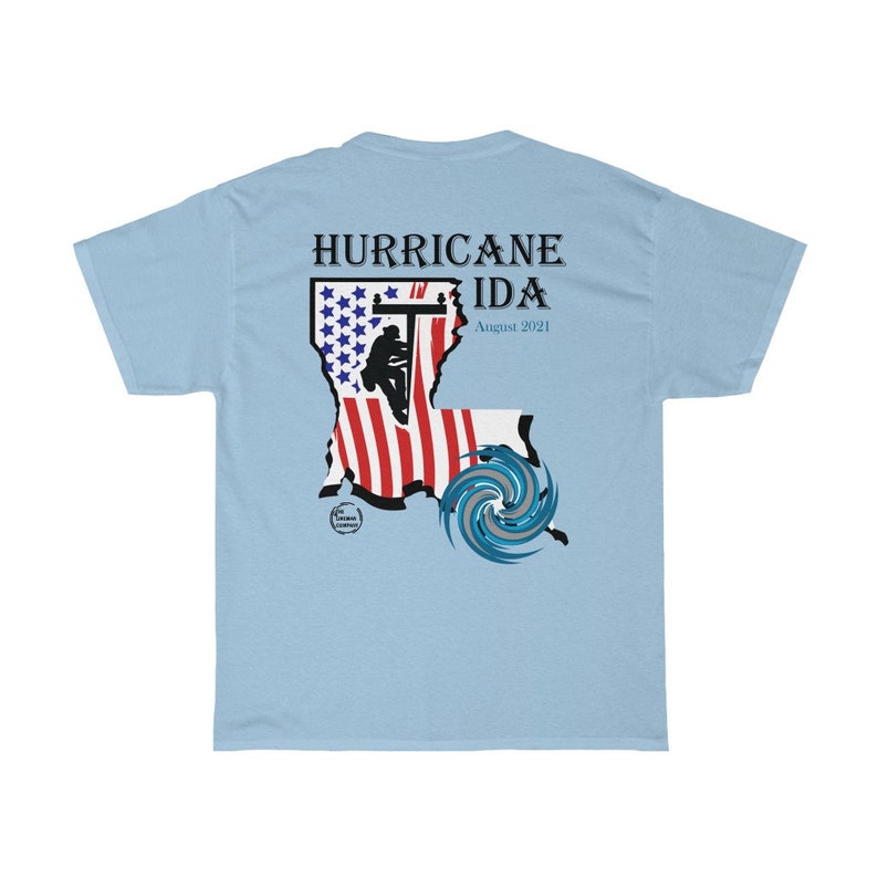 Pu&ograve; includere: T-shirt azzurra con una grafica che commemora l'uragano Ida. Il design include il testo "HURRICANE IDA August 2021" sopra una mappa stilizzata della Louisiana con un design a bandiera americana e una grafica di uragano.