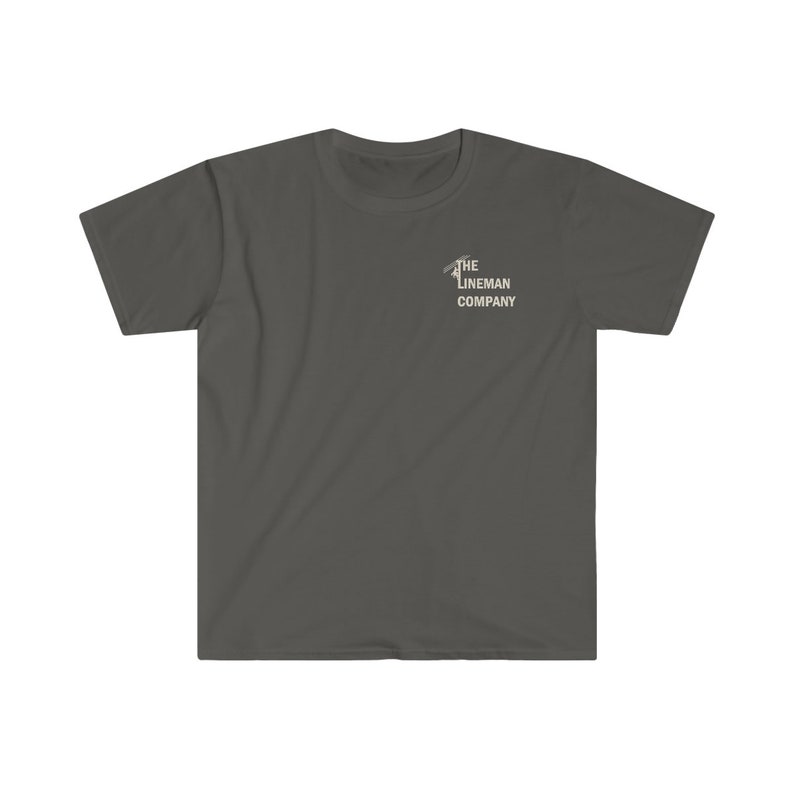 Op de afbeelding: Een donkergrijs T-shirt met een witte afbeelding van een monteur die een elektriciteitsmast beklimt. De afbeelding bevat de tekst "The Lineman Company".