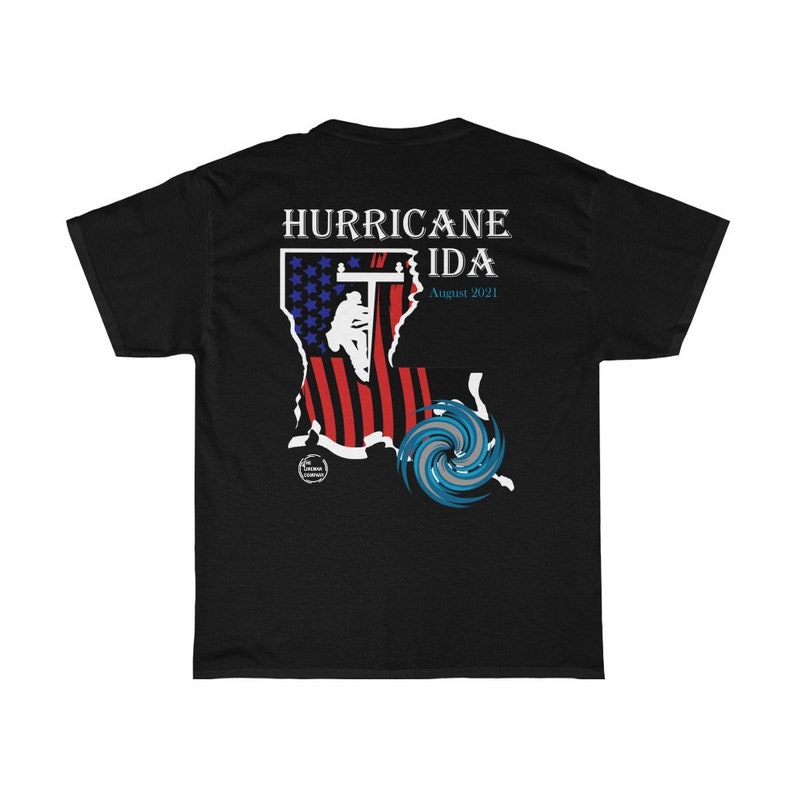 Pu&ograve; includere: T-shirt nera con la scritta "HURRICANE IDA August 2021". Il design include una mappa stilizzata della Louisiana con la bandiera americana e una grafica di uragano blu e bianca. La maglietta ha maniche corte e girocollo.