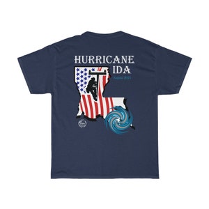 Pu&ograve; includere: T-shirt blu navy con la scritta "HURRICANE IDA August 2021". Il design include la sagoma di un elettricista su un palo della luce all'interno del contorno della Louisiana, con una grafica stilizzata dell'uragano.