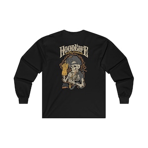 Pode incluir: Camiseta preta de manga comprida com um gr&aacute;fico de um esqueleto usando uma m&aacute;scara de soldador e segurando um ma&ccedil;arico de solda. O texto "HOODLIFE BLUE COLLAR REBELLION ESTD. MMXX" est&aacute; impresso na camiseta.