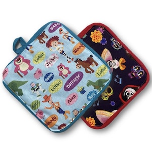 Può includere: Due presine quadrate. Una è azzurra con personaggi dei cartoni animati e l'altra è blu scuro con teschi e fiori. Entrambe hanno un anello per appenderle e sono rifinite con un colore a contrasto.