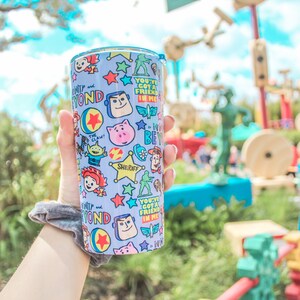 K&ouml;nnte beinhalten: Ein blauer und wei&szlig;er wiederverwendbarer Becher mit Toy Story-Motiv. Der Becher zeigt Figuren wie Woody, Buzz Lightyear und Jessie. Der Text auf dem Becher lautet "You've Got a Friend in Me".