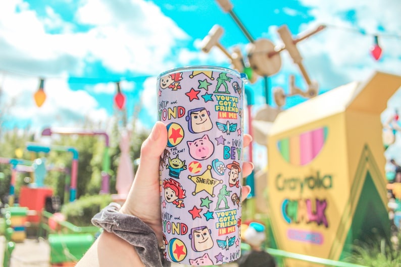 K&ouml;nnte beinhalten: Ein lila-wei&szlig;er Edelstahlbecher mit Toy Story-Motiv. Der Becher ist mit Bildern von Woody, Buzz Lightyear und anderen Figuren aus dem Film bedeckt. Der Text "You've got a friend in me" ist auf dem Becher aufgedruckt.