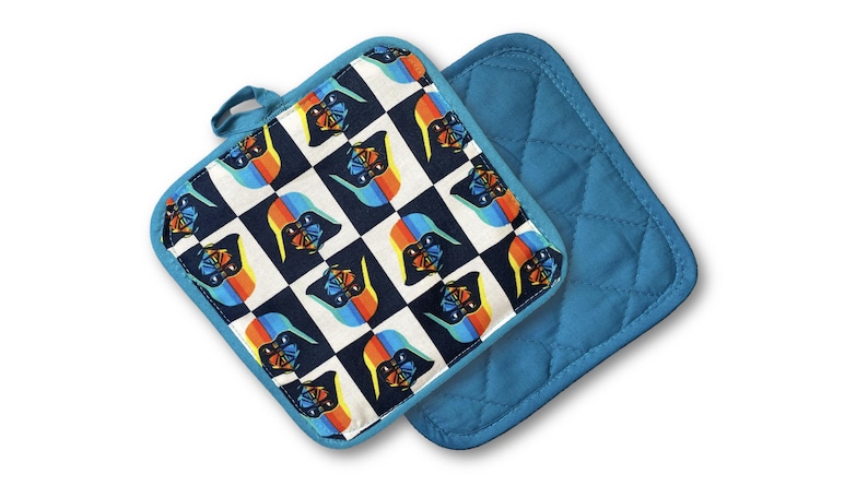 May include: Two square pot holders. One features a checkered pattern with a character design in black, blue, orange, and white. The other is solid blue with a quilted design. Both have blue trim and a hanging loop.
