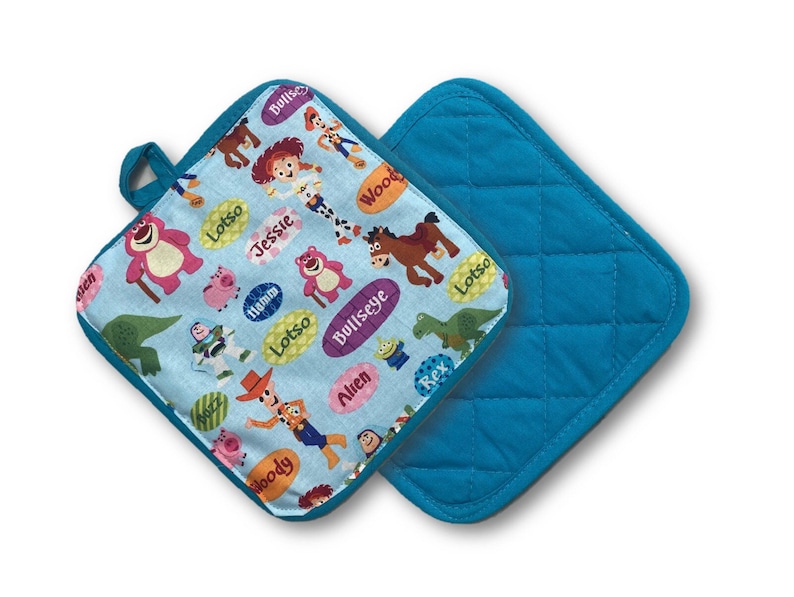 May include: Two square pot holders. One features a light blue background with cartoon characters and character names. The other is solid teal with a quilted pattern. Both have teal trim and a teal loop for hanging.