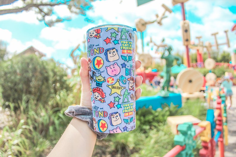 K&ouml;nnte beinhalten: Ein blauer und wei&szlig;er wiederverwendbarer Becher mit Toy Story-Motiv. Der Becher zeigt Figuren wie Woody, Buzz Lightyear und Jessie. Der Text auf dem Becher lautet "You've Got a Friend in Me".