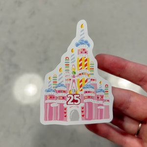 May include: A pink and white sticker of a birthday cake version of the Cinderella Castle with the number 25 on the front.