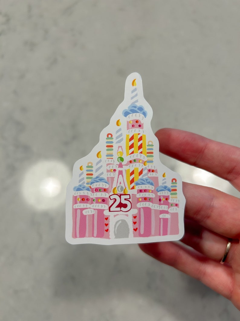 May include: A pink and white sticker of a birthday cake version of the Cinderella Castle with the number 25 on the front.