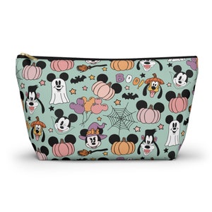 May include: A light teal cosmetic bag with a gold zipper, featuring a Halloween-themed pattern. The pattern includes Mickey Mouse, Minnie Mouse, Goofy, pumpkins, ghosts, bats, stars, and the word "BOO!"