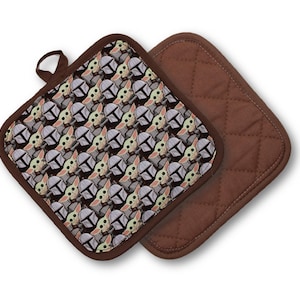 May include: Two square pot holders. One features a repeating pattern of a character's face with a helmet, in shades of gray, tan, and green. The other is solid brown with a quilted design. Both have brown trim.
