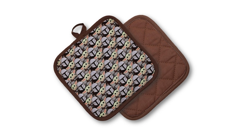 May include: Two square pot holders. One features a repeating pattern of a character's face with a helmet, in shades of gray, tan, and green. The other is solid brown with a quilted design. Both have brown trim.