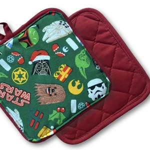 May include: Two square pot holders. One is a quilted solid burgundy. The other is green with Star Wars characters and holiday icons. The pot holder has a burgundy trim and a loop for hanging.