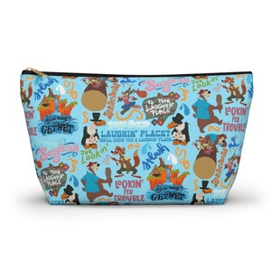 May include: A light blue zippered pouch featuring a repeating pattern of cartoon characters and phrases like "Laughin' Place" and "Get Wet." The pouch has a black zipper and a gold-colored pull.