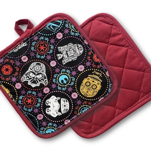 May include: Two square pot holders. One features a black background with colorful Day of the Dead-style Star Wars character designs. The other is solid red with a quilted pattern. Both have red trim and a hanging loop.