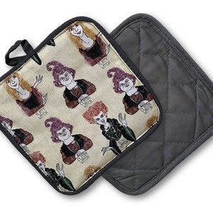 Puede incluir: Un par de guantes para horno con una parte posterior acolchada negra y una parte delantera de tela beige con un patr&oacute;n repetido de brujas de dibujos animados con el texto "Clever Witch" y "Pretty Witch".