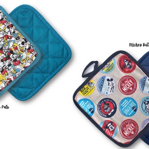 May include: Two quilted pot holders with a Mickey Mouse theme. One pot holder features a blue background with a white and yellow pattern of Mickey Mouse and his friends. The other pot holder features a beige background with a red, blue, and yellow pattern of Mickey Mouse buttons. Both pot holders have a dark blue quilted back.