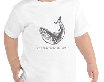 May include: White toddler t-shirt with a black and white illustration of a whale jumping out of the water. The text "SEE WORLD OCEANS FISH JUMP" is printed below the whale.