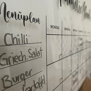 May include: A white dry-erase board with a black marker listing a weekly meal plan. The meal plan includes "Chilli", "Greek Salad", "Burger", "Potato", and "Arts". The board also has a calendar with the days of the week labeled in German: "Montag" (Monday), "Dienstag" (Tuesday), and "Mittwoch" (Wednesday).