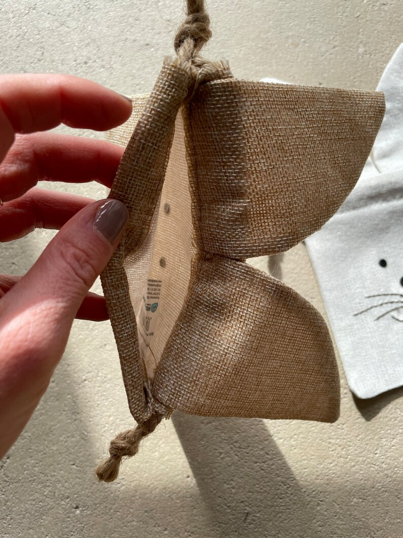 Puede incluir: Una peque&ntilde;a bolsa de arpillera marr&oacute;n con cierre de cord&oacute;n. La bolsa est&aacute; abierta y el interior es visible. La bolsa est&aacute; hecha de fibras naturales y tiene un aspecto r&uacute;stico.
