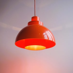 Könnte beinhalten: Eine leuchtend orangefarbene Pendelleuchte mit einem mehrschichtigen, kuppelförmigen Schirm.