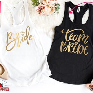 May include: Two white tank tops with gold lettering. One says "Bride" with a diamond graphic. The other says "Team Bride" with a heart graphic.