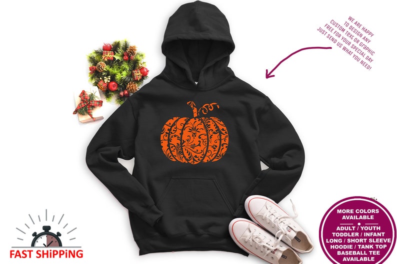 May include: Black hoodie featuring an orange pumpkin design. The pumpkin is filled with a black and white floral pattern. The hoodie has a drawstring hood and a kangaroo pocket.