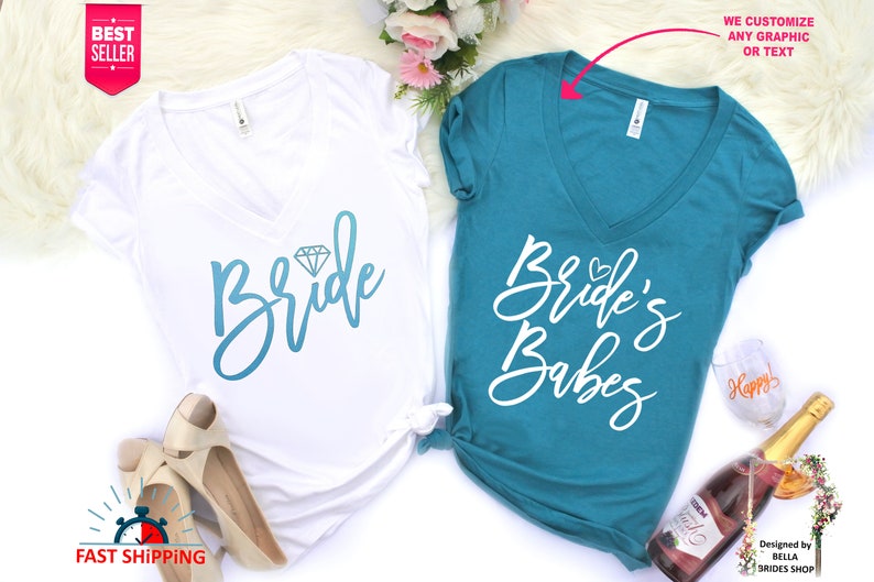May include: Two white v-neck t-shirts with a blue and white graphic design. The shirt on the left says "Bride" with a diamond graphic. The shirt on the right says "Bride's Babes".
