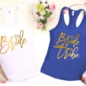 May include: Two white tank tops with gold lettering. The top on the left says "Bride" with a diamond graphic. The top on the right says "Bride Tribe".
