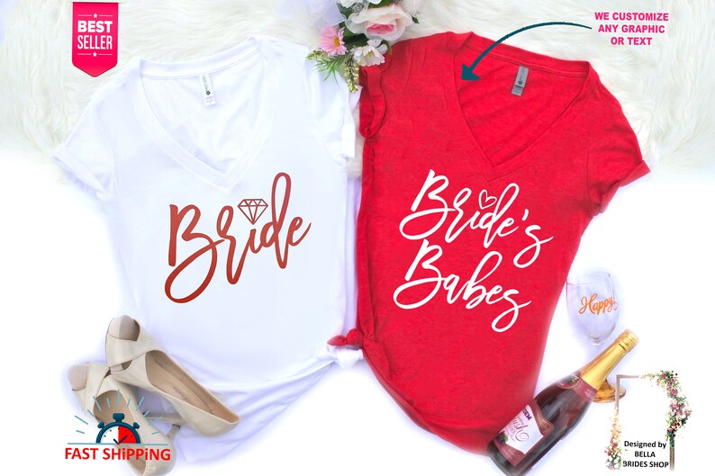 May include: Two white v-neck t-shirts with a red and white design. The shirt on the left says "Bride" with a diamond graphic. The shirt on the right says "Bride's Babes".