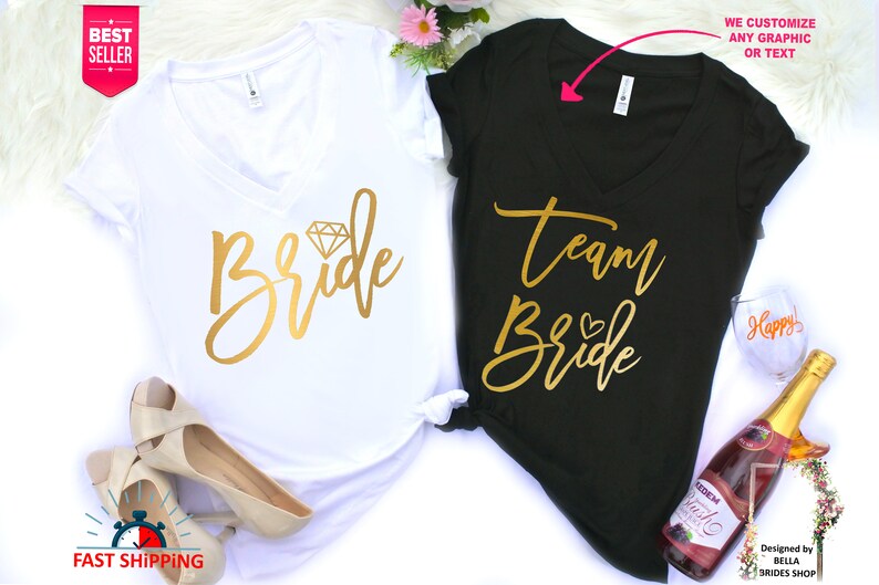 May include: Two white and black t-shirts with gold lettering. The white shirt says "Bride" with a diamond graphic. The black shirt says "Team Bride" with a small heart graphic.