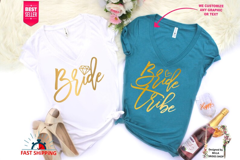 May include: Two white v-neck t-shirts with gold lettering. One shirt says "Bride" with a diamond graphic. The other shirt says "Bride Tribe".