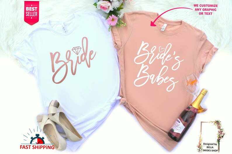 May include: Two white t-shirts with a pink and white design. The first shirt says "Bride" with a diamond graphic. The second shirt says "Bride's Babes".
