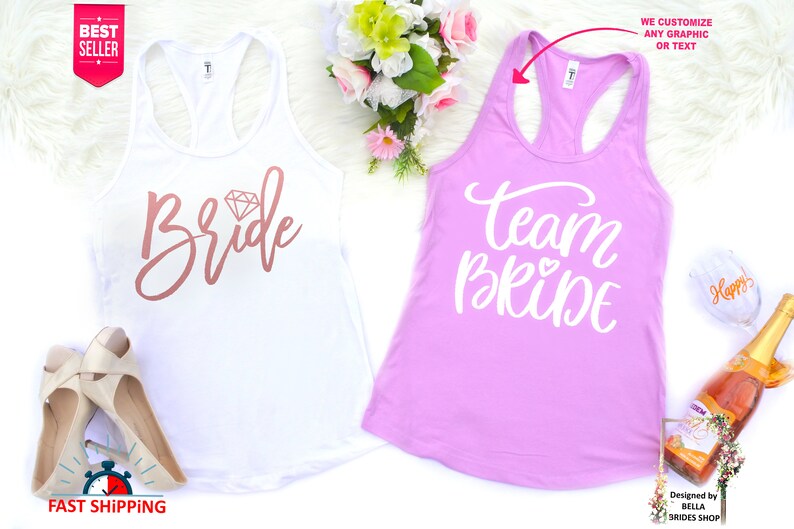 May include: Two white tank tops with the words "Bride" and "Team Bride" printed on them. The "Bride" tank top has a pink diamond graphic. The "Team Bride" tank top is pink.