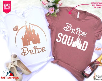 May include: Two t-shirts with a Disney castle graphic. The white t-shirt says "Bride" in gold lettering and has a diamond ring graphic. The pink t-shirt says "Bride Squad" in white lettering.
