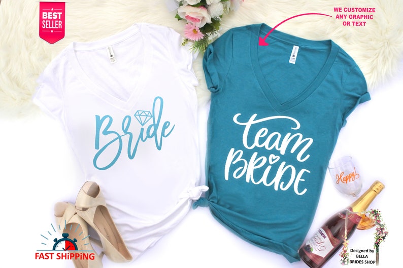 May include: Two white v-neck t-shirts with blue text. One shirt says "Bride" with a diamond graphic. The other shirt says "Team Bride" with a small heart graphic.