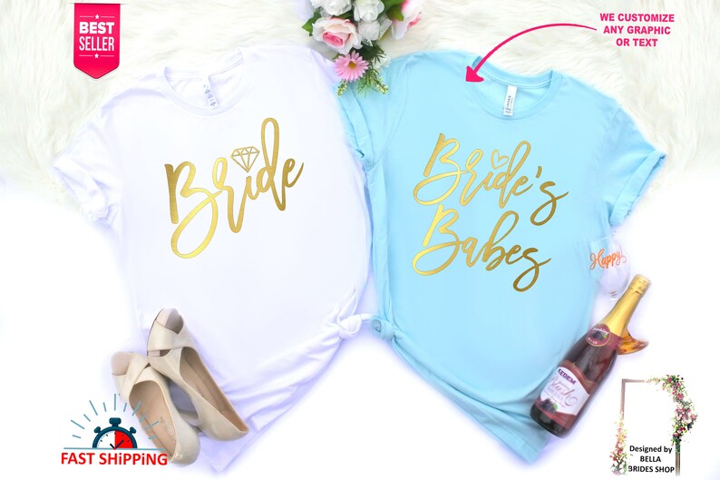 May include: Two white t-shirts with gold lettering. The first shirt says "Bride" with a diamond graphic. The second shirt says "Bride's Babes".