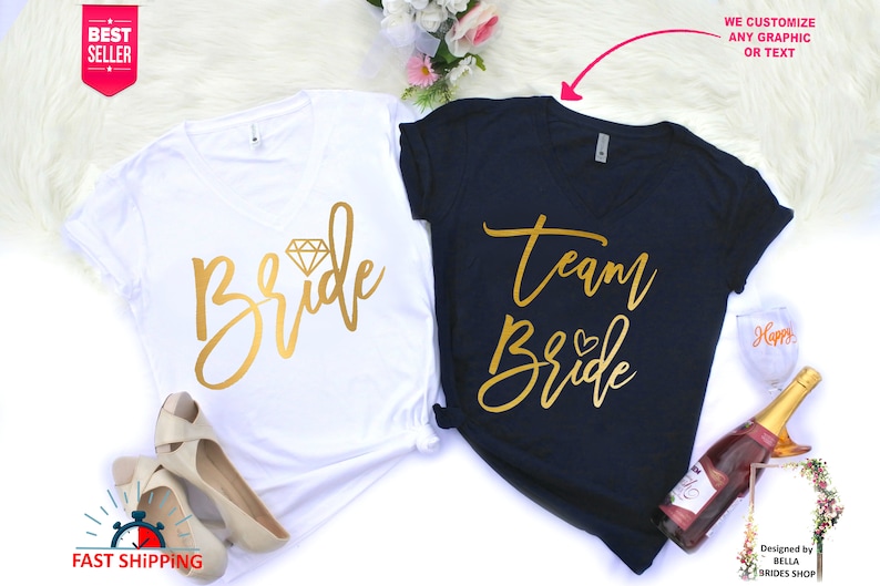 May include: Two white and navy blue t-shirts with gold lettering. The white t-shirt says "Bride" with a diamond graphic. The navy blue t-shirt says "Team Bride" with a heart graphic.