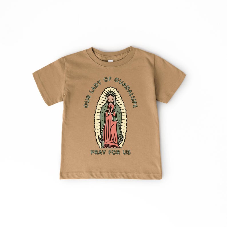 May include: Tan short-sleeve t-shirt featuring a graphic of Our Lady of Guadalupe. The illustration is in a vintage style, with the text "OUR LADY OF GUADALUPE" and "PRAY FOR US" surrounding the image.