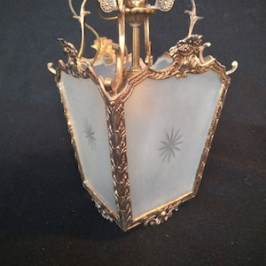 Puede incluir: Una lámpara colgante de metal dorado con una pantalla de vidrio esmerilado. La pantalla tiene un diseño de estrella y la lámpara tiene detalles ornamentados.