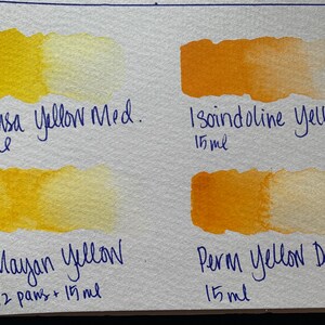 May include: Four watercolor paint swatches on a white surface. The swatches are labeled "Hansa Yellow Med. 5ml", "Mayan Yellow 1/2 pans + 15ml", "Isoindoline Yellow 15ml", and "Perm Yellow Deep 15ml".