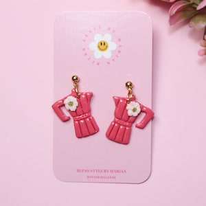 May include: Pink ceramic earrings shaped like a coffee pot with a white flower detail. The earrings are on a white card with the text "Bless Style by Marian Winterhaven FL".