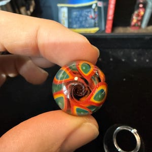May include: A colorful glass marble with a swirling pattern of red, green, and blue. The marble has a clear center with a dark brown swirl.