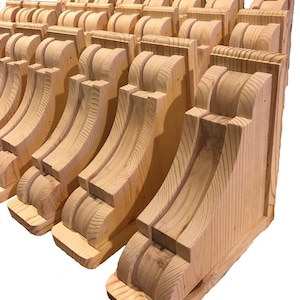 May include: A row of unfinished wooden corbels, stacked and arranged in a staggered pattern. The corbels are made of light-colored wood and have a simple, elegant design.