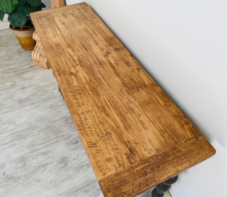 Peut inclure: Une console en bois longue avec une finition en bois naturel. La table a un dessus rectangulaire simple et une base sculpt&eacute;e et enroul&eacute;e.
