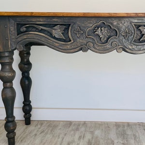 Peut inclure: Une console en bois gris fonc&eacute; avec des d&eacute;tails sculpt&eacute;s complexes et des pieds tourn&eacute;s. La table a un dessus l&eacute;g&egrave;rement incurv&eacute; et une finition vieillie.