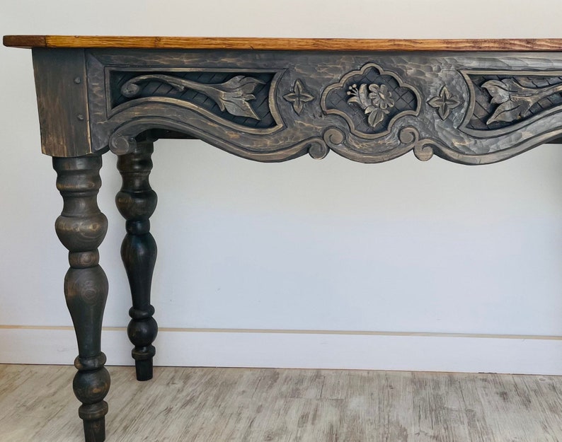 Peut inclure: Une console en bois gris fonc&eacute; avec des d&eacute;tails sculpt&eacute;s complexes et des pieds tourn&eacute;s. La table a un dessus l&eacute;g&egrave;rement incurv&eacute; et une finition vieillie.