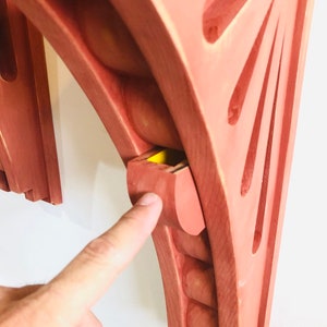 May include: A wooden wall shelf with a unique design featuring a curved top and a small hidden compartment. The shelf is painted a light reddish-brown color.