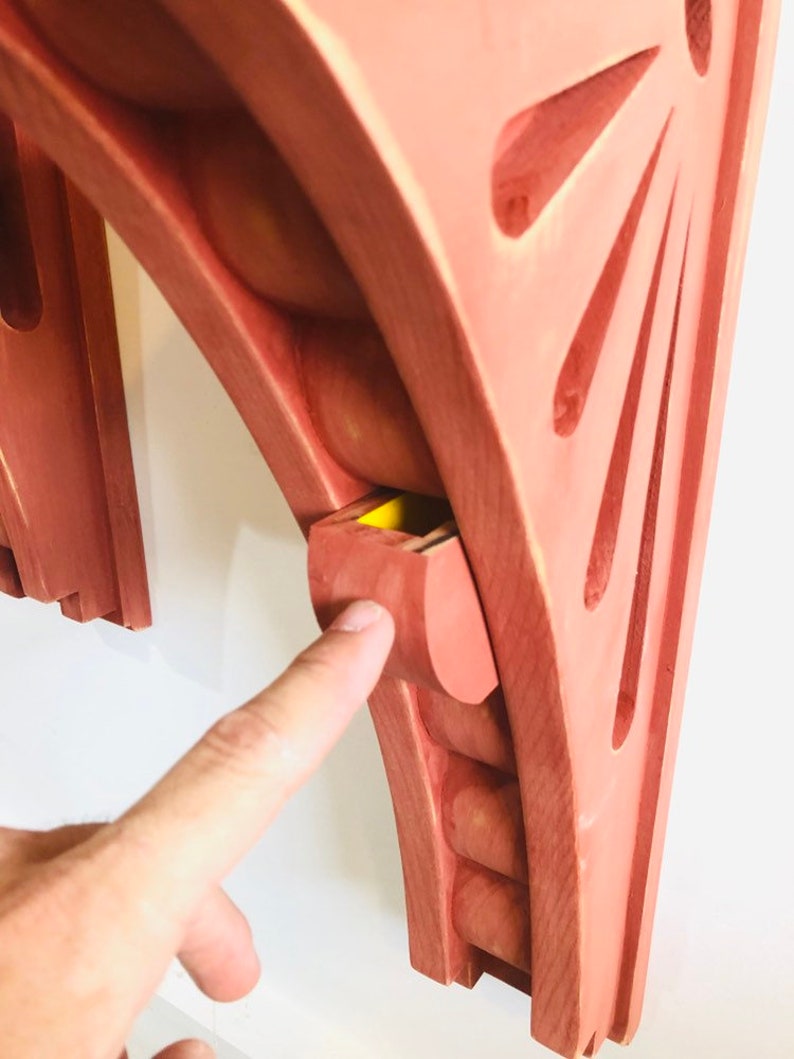 May include: A wooden wall shelf with a unique design featuring a curved top and a small hidden compartment. The shelf is painted a light reddish-brown color.