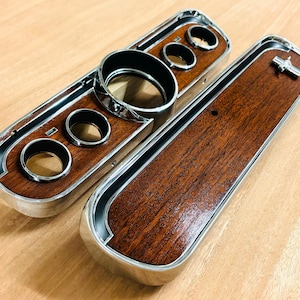 May include: A set of two woodgrain dashboard panels for a classic car. The panels are chrome-plated and have a woodgrain finish. The panels are designed to fit a 1965-1966 Ford Mustang.
